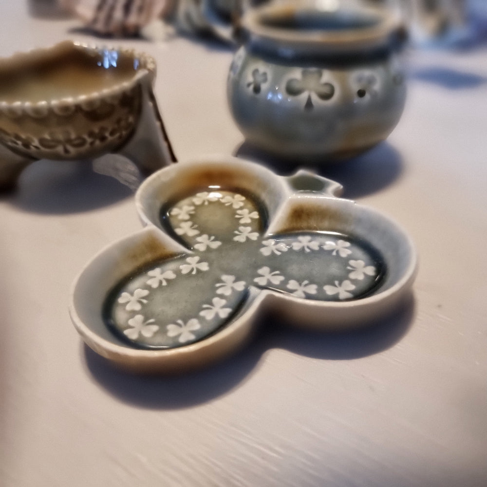 Trio of vintage Wade shamrock dishes in grey-blue glaze with honey brown highlights, including a footed dish, a pierced pot with wire handle, and a clover-shaped dish