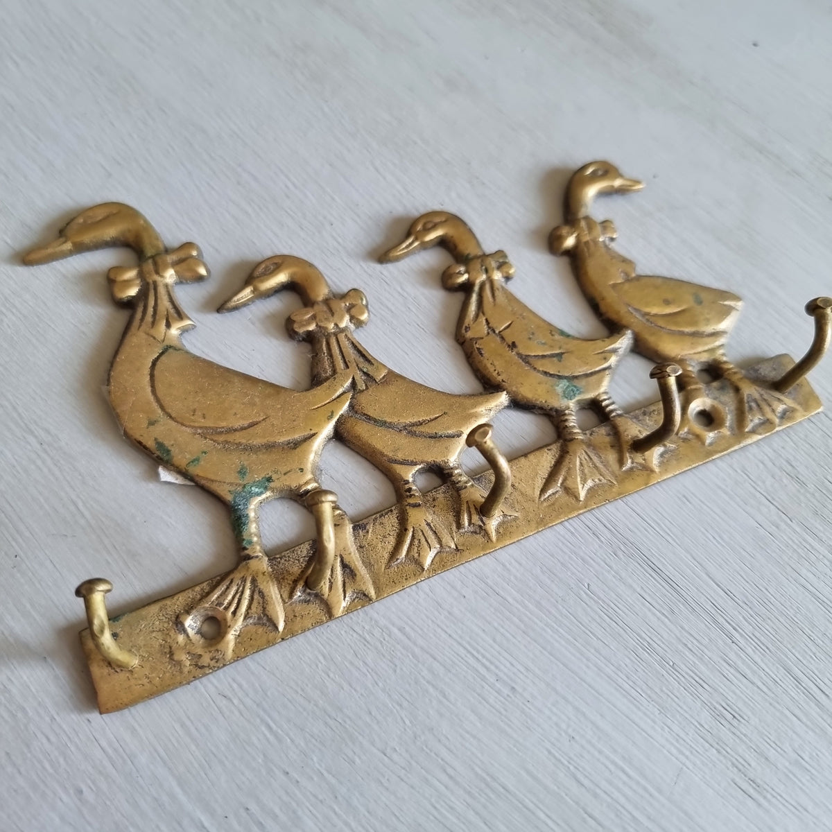 Vintage brass key hook shaped as four ducks with bows in a row, with three hooks along the base