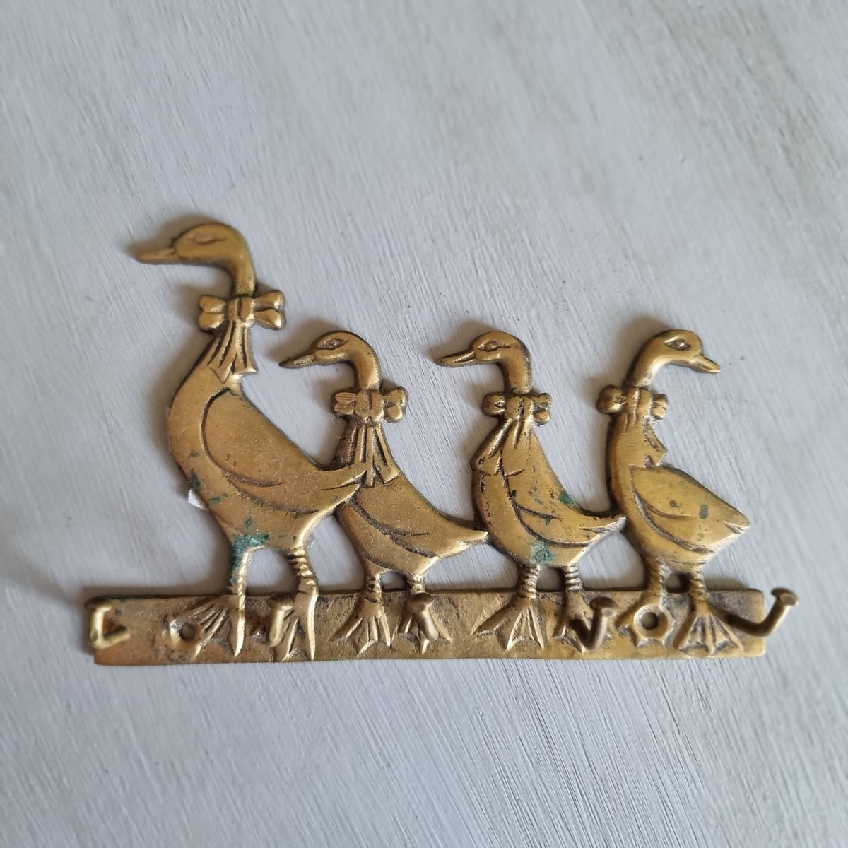 Vintage brass key hook shaped as four ducks with bows in a row, with three hooks along the base