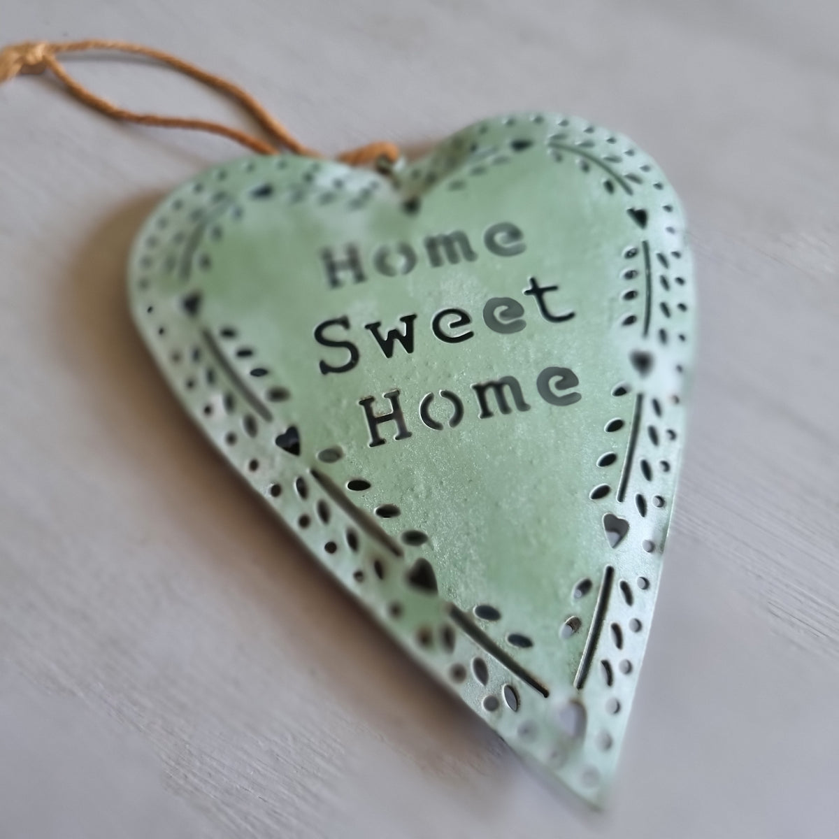 Sage green metal heart with Home Sweet Home cut out in the centre and a punched heart and leaf border, hanging from twine