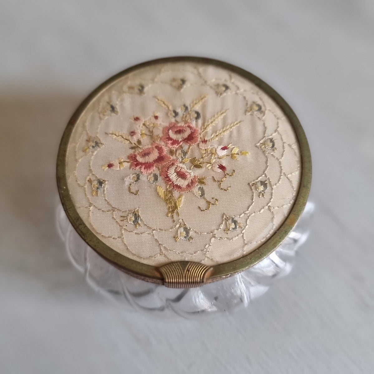 Vintage swirled clear glass jar with a gold-tone lid featuring embroidered pink roses on cream fabric