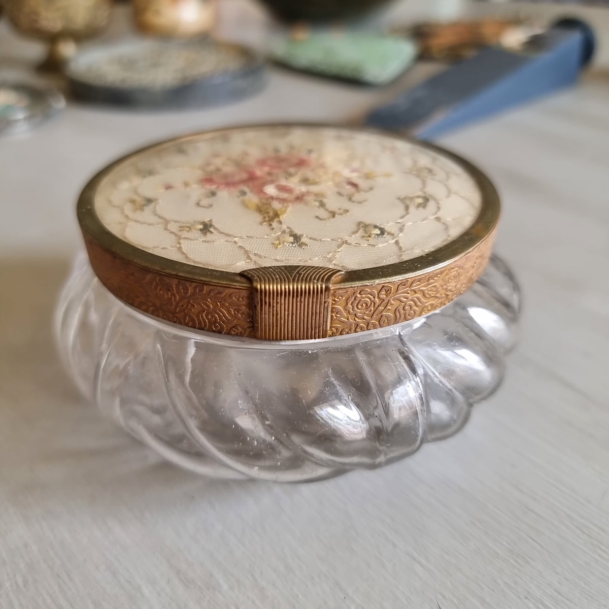 Vintage swirled clear glass jar with a gold-tone lid featuring embroidered pink roses on cream fabric