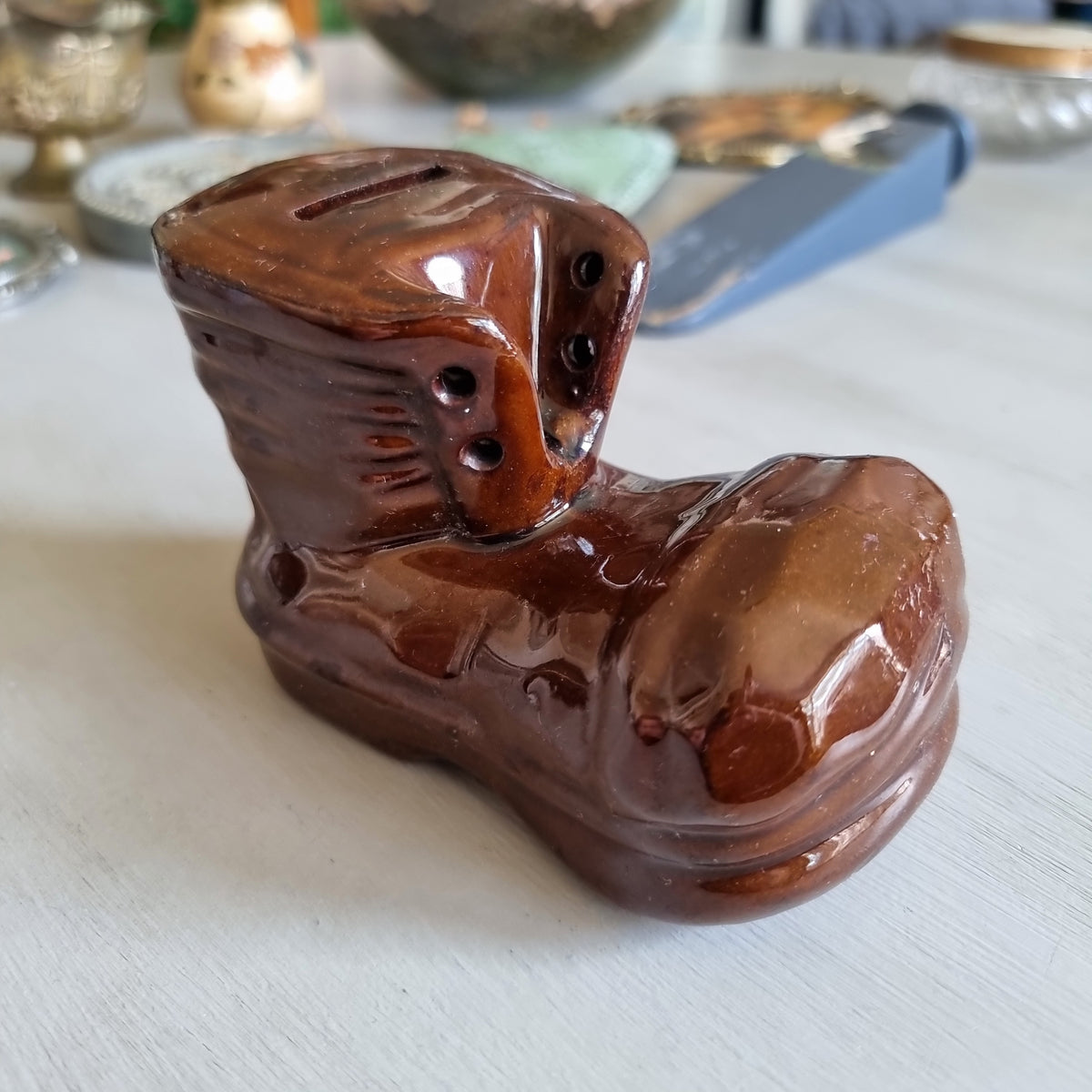 Glossy brown glazed pottery money box shaped like a lace-up boot with a coin slot in the top