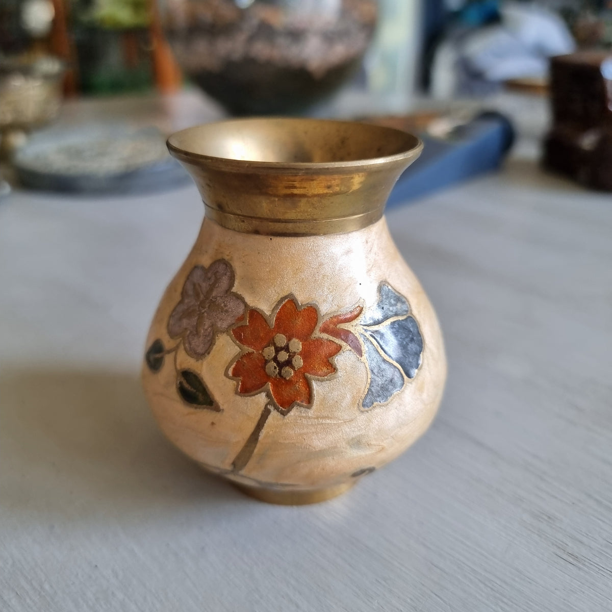 Small brass bud vase with a cream enamel body decorated with rust red, blue and grey flowers