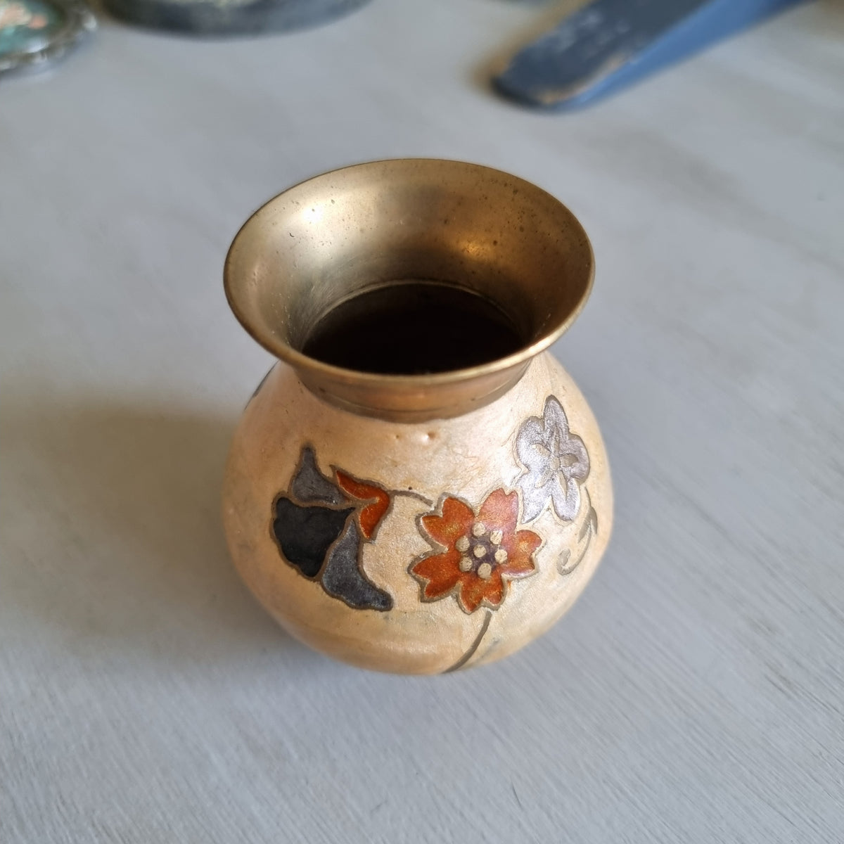 Small brass bud vase with a cream enamel body decorated with rust red, blue and grey flowers