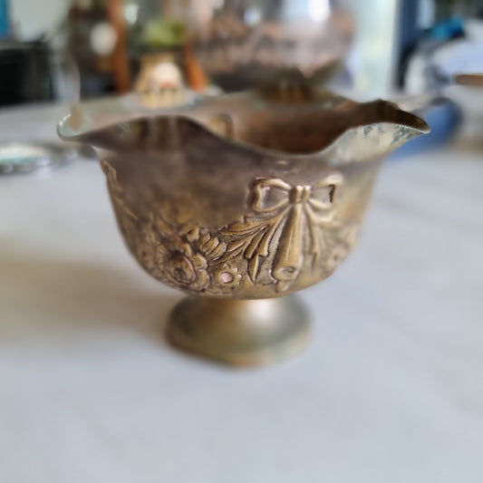 Small silver plated footed bowl with a ruffled rim, embossed with ribbon bows and roses, showing an aged patina