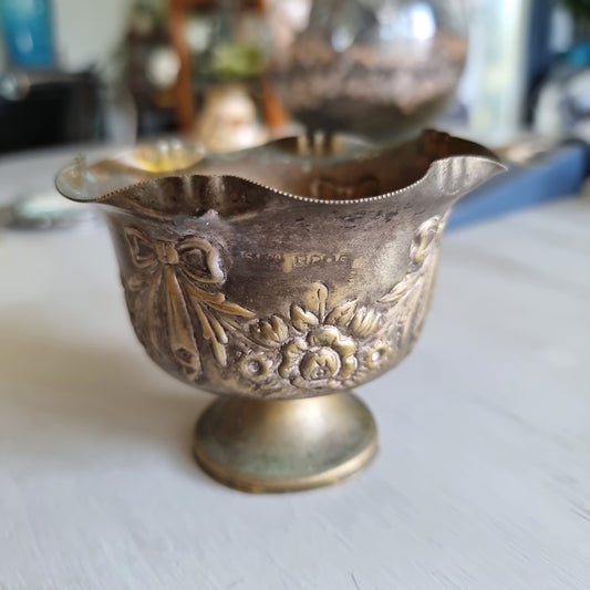 Small silver plated footed bowl with a ruffled rim, embossed with ribbon bows and roses, showing an aged patina