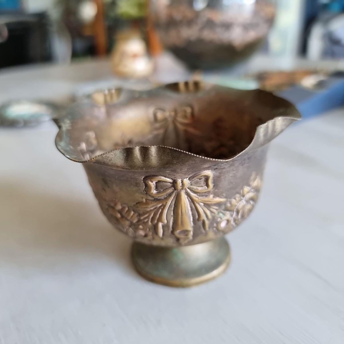 Small silver plated footed bowl with a ruffled rim, embossed with ribbon bows and roses, showing an aged patina