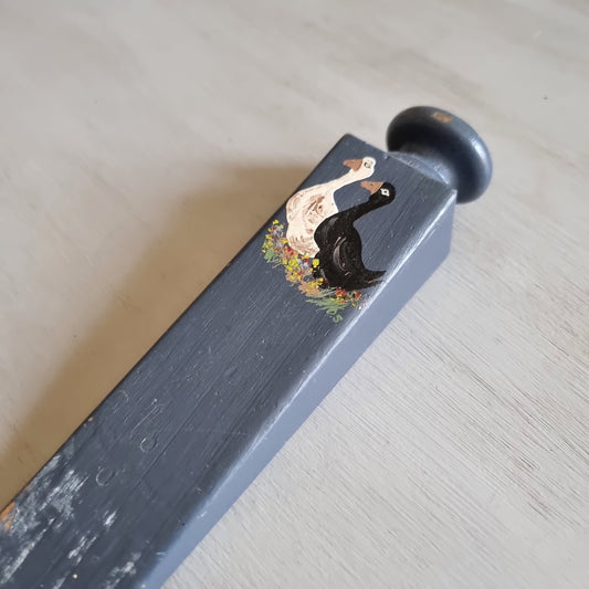 Grey painted wooden wedge door stop with a round knob, hand painted with a white goose and a black goose among flowers
