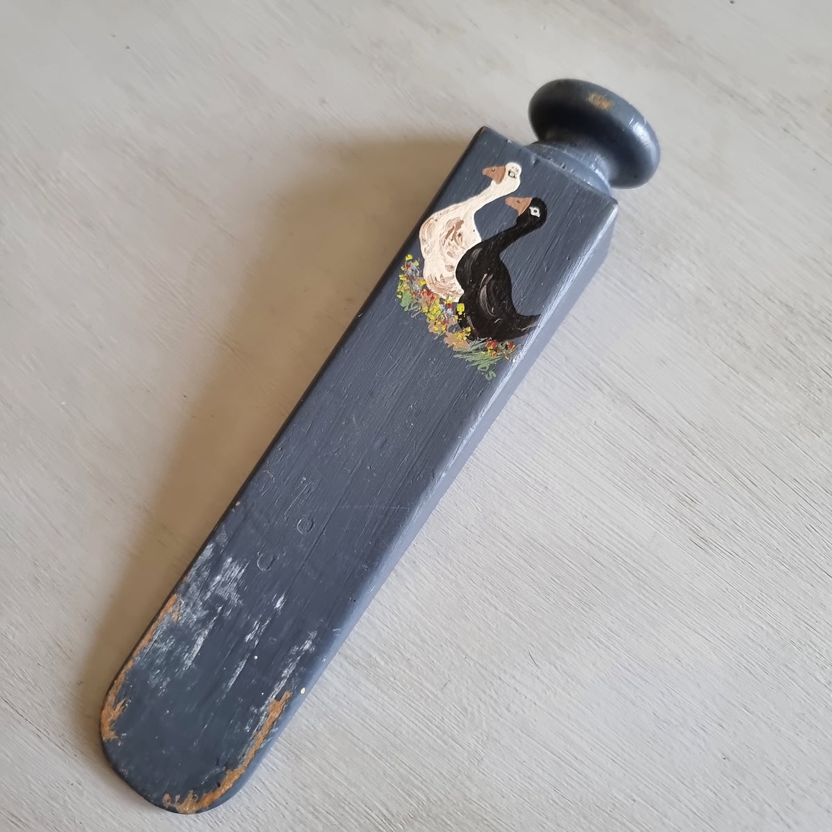 Grey painted wooden wedge door stop with a round knob, hand painted with a white goose and a black goose among flowers