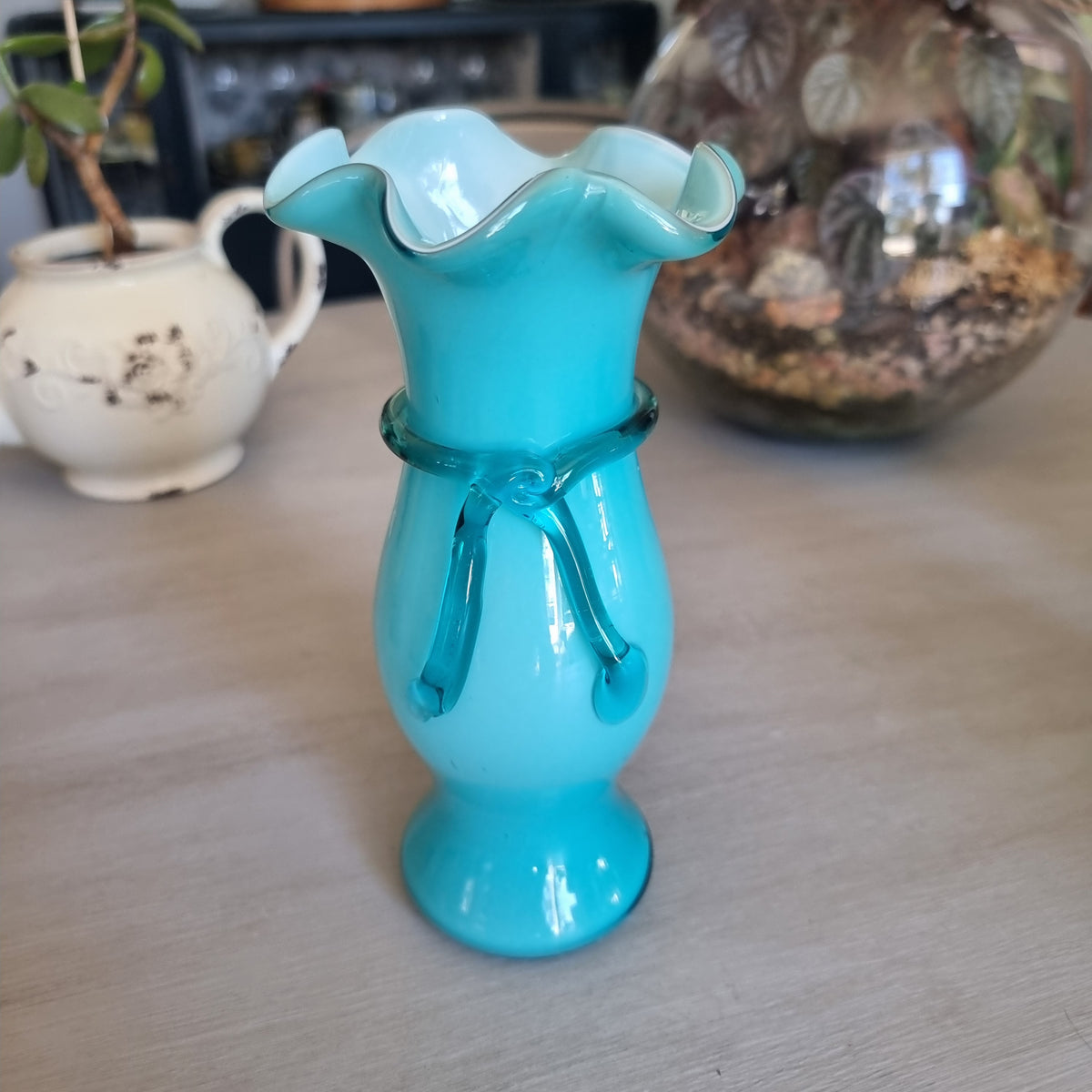 Vintage teal cased glass vase with a ruffled rim and glass ribbon tied in a bow around the neck