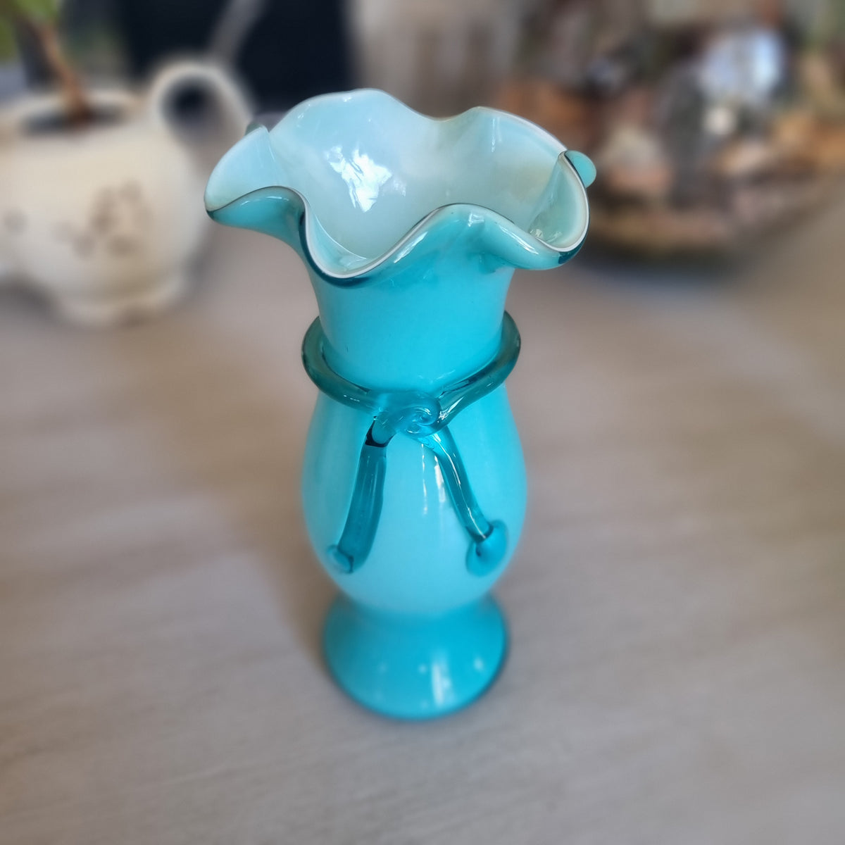 Vintage teal cased glass vase with a ruffled rim and glass ribbon tied in a bow around the neck