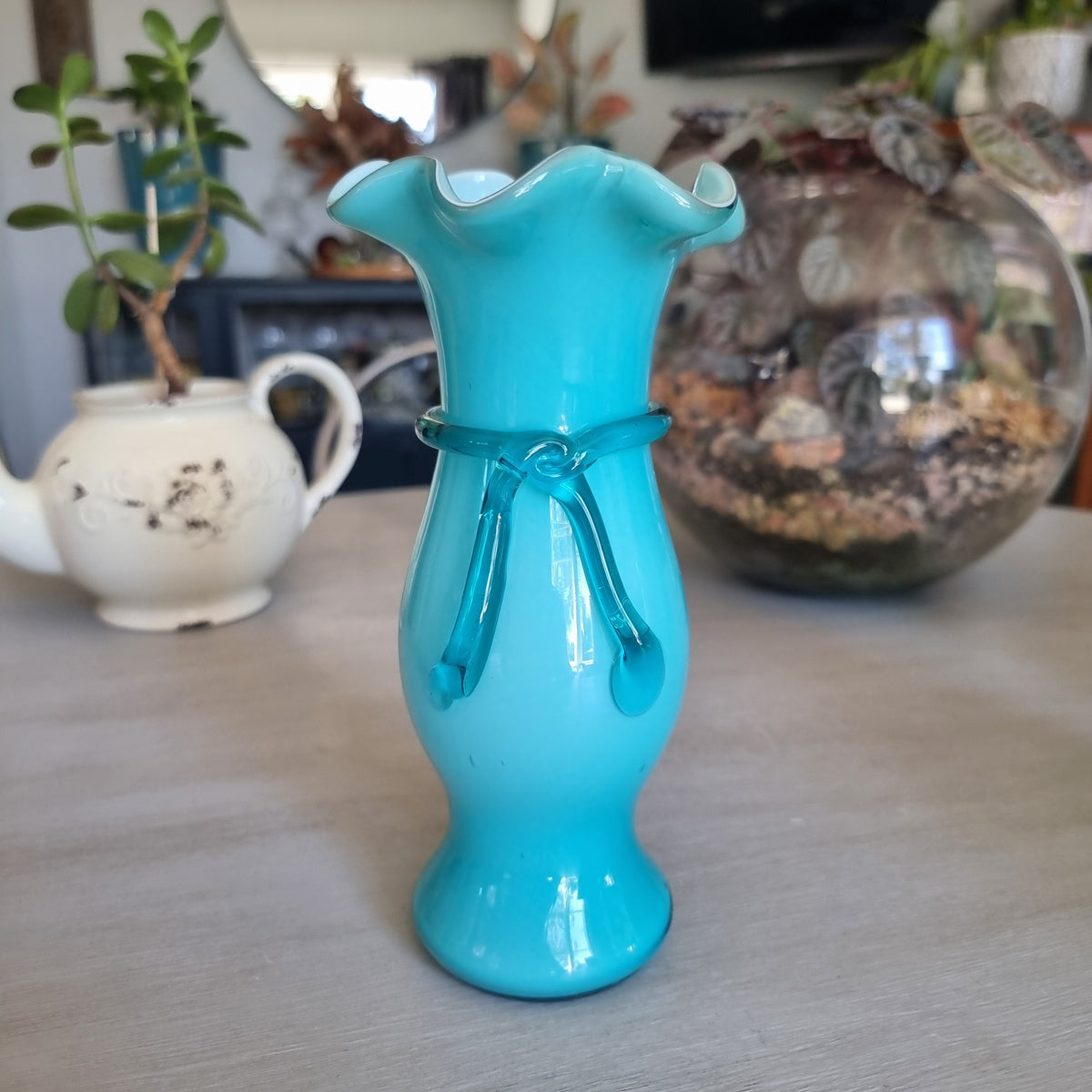 Vintage teal cased glass vase with a ruffled rim and glass ribbon tied in a bow around the neck