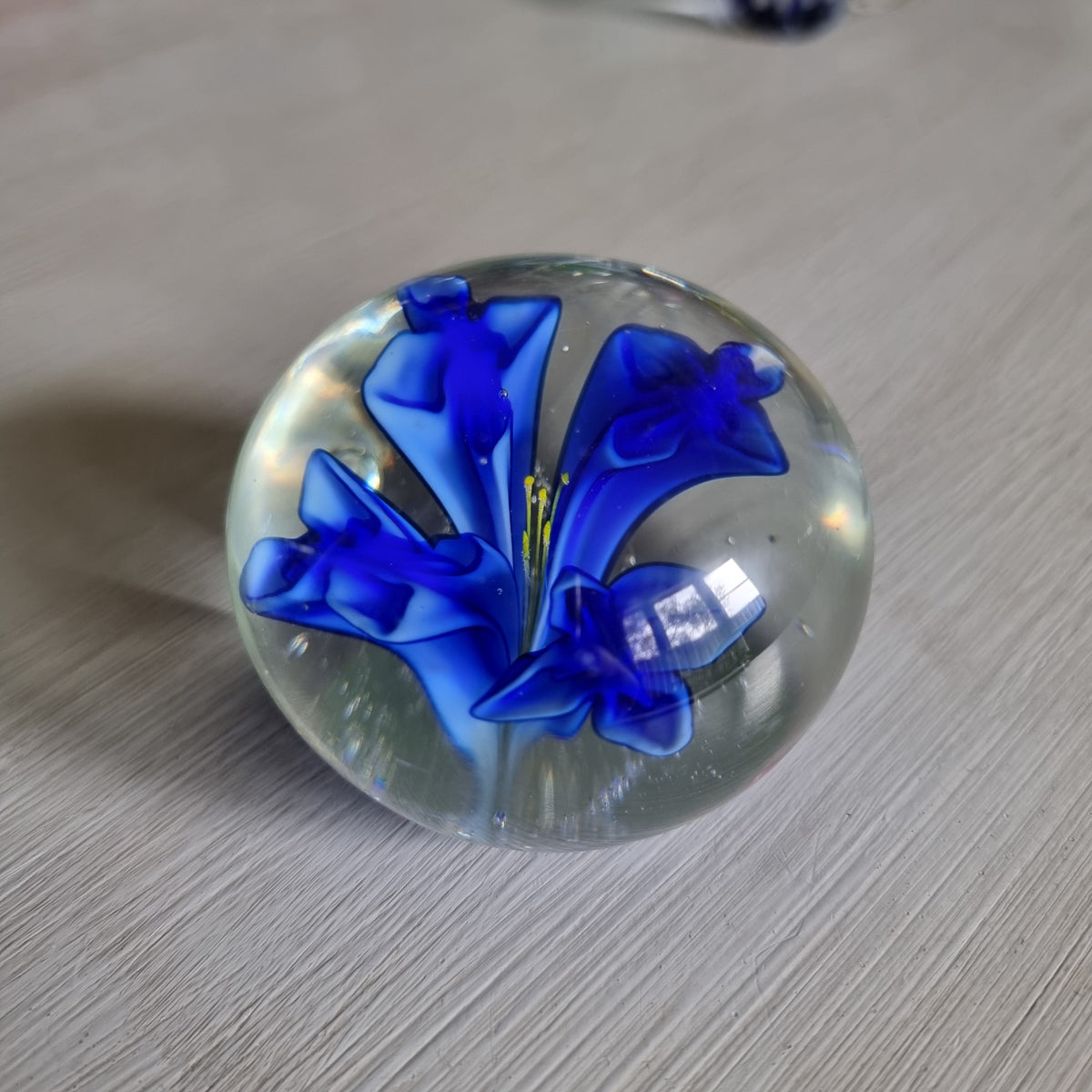 Clear glass paperweight with blue flower and yellow centre