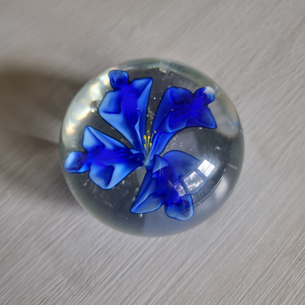 Clear glass paperweight with blue flower and yellow centre