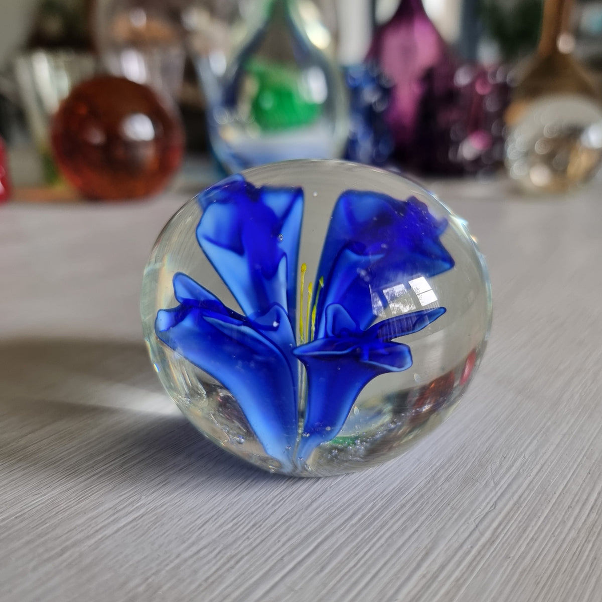 Clear glass paperweight with blue flower and yellow centre