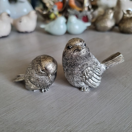 Two textured antique silver-tone metal birds, one looking up and one with head tucked down