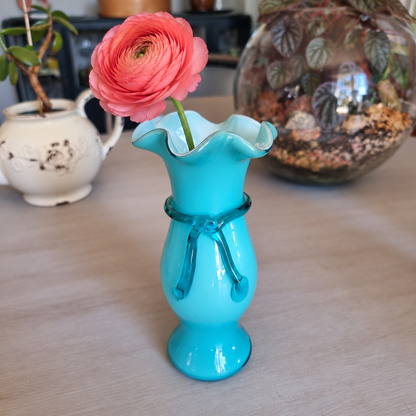 Vintage teal cased glass vase with a ruffled rim and bow detail holding a coral ranunculus