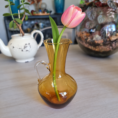 Vintage amber glass jug vase with a clear handle holding a single pink tulip