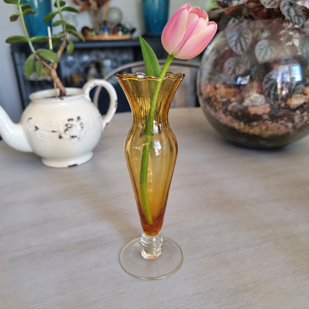 Vintage amber glass footed bud vase with a scalloped rim holding a single pink tulip
