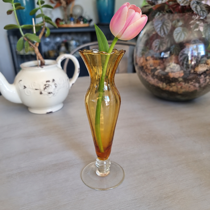 Vintage amber glass footed bud vase with a scalloped rim holding a single pink tulip