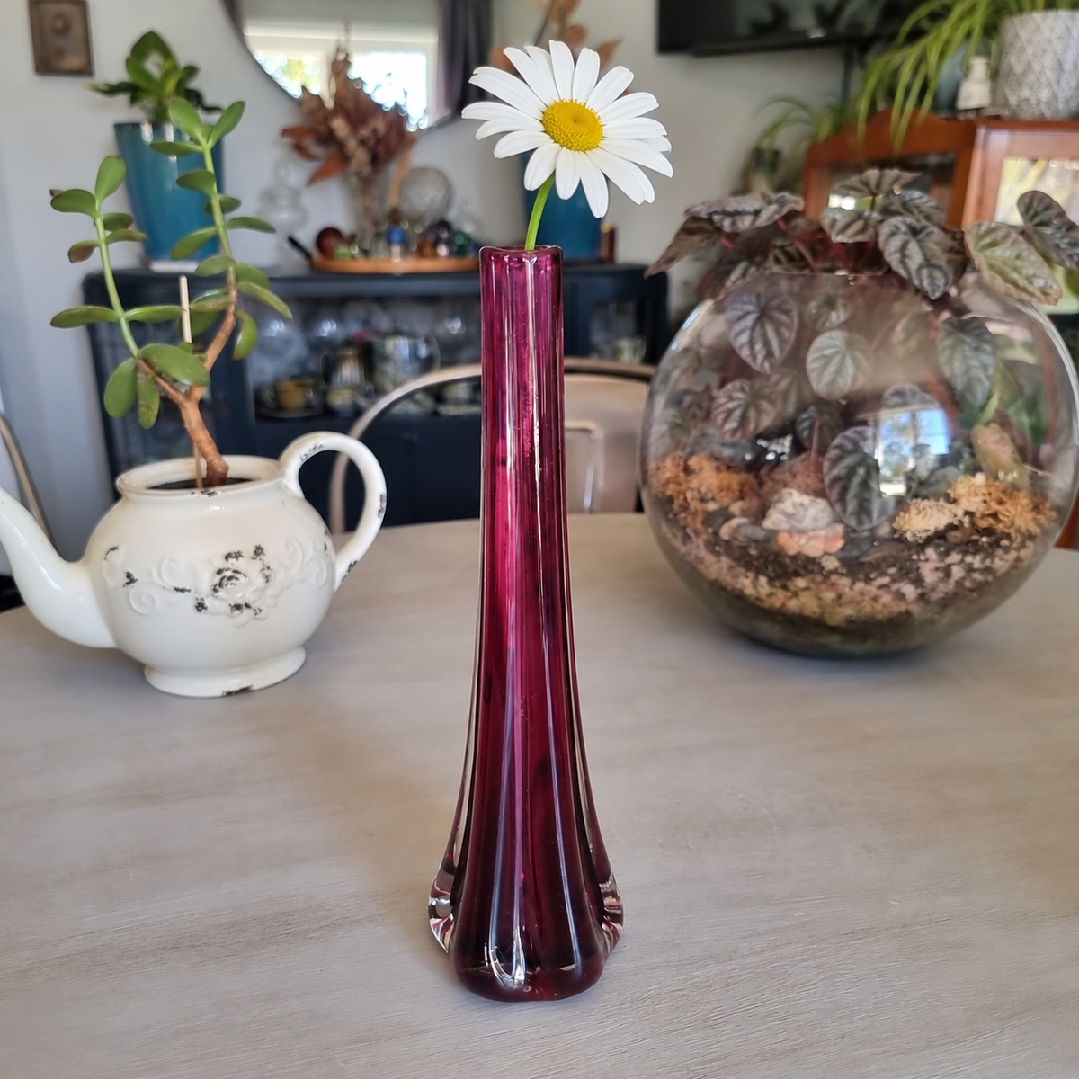 Tall vintage purple glass bud vase with a clear base holding a single white daisy