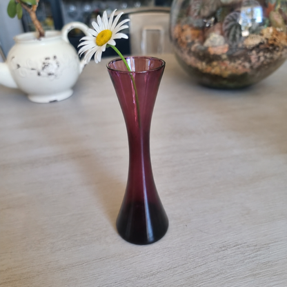 Small vintage purple glass hourglass bud vase holding a single white daisy